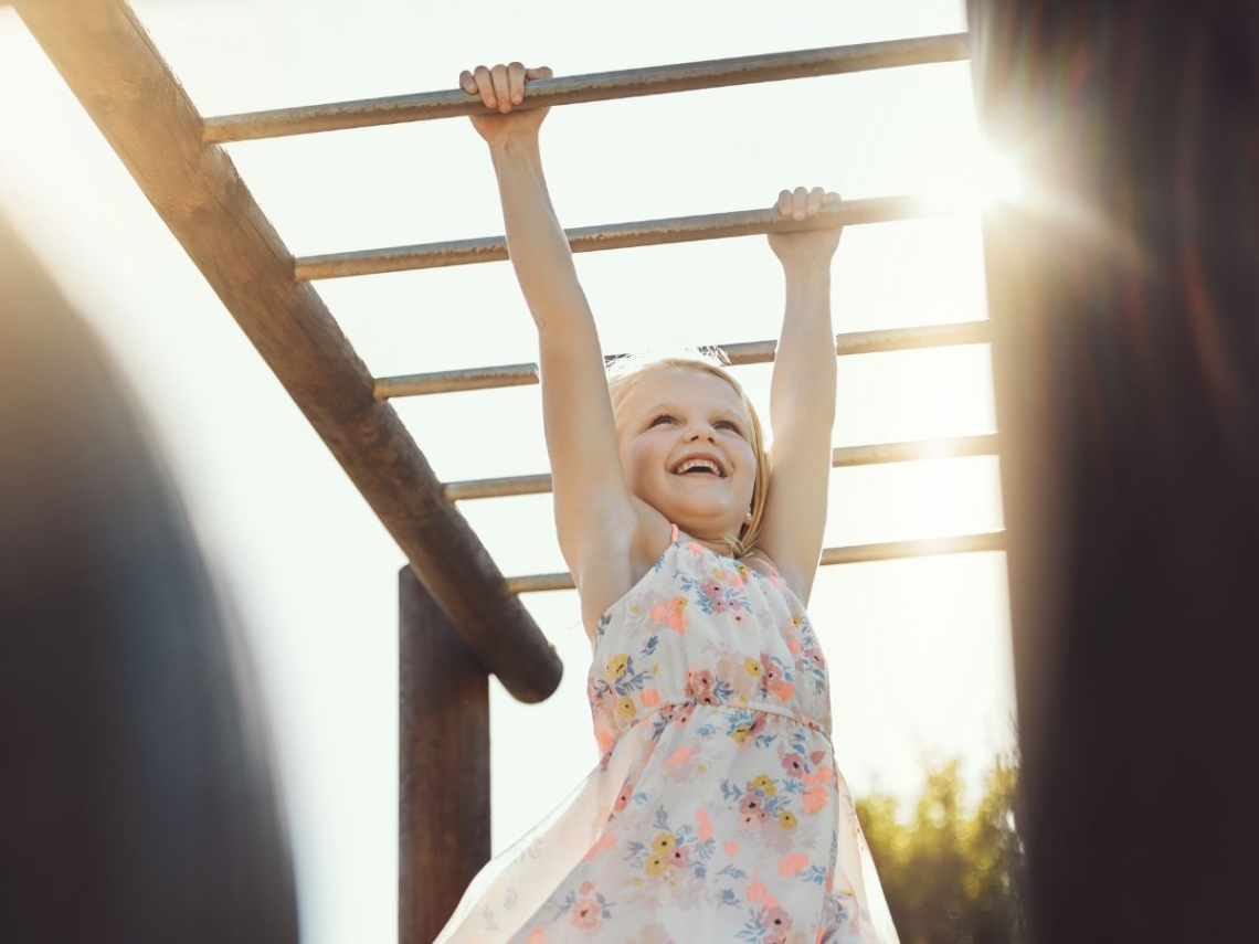 a young girl smiling while hanging from monkey bars.jpg