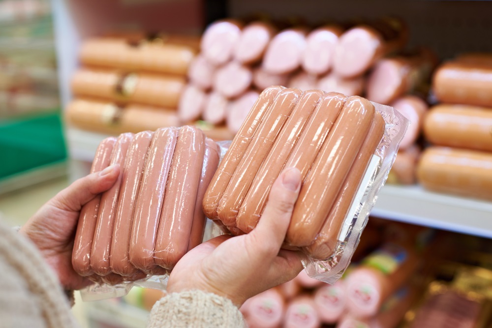 Shopping holding up two packages of processed sausages in deli aisle