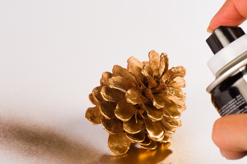 A pinecone being spray painted gold