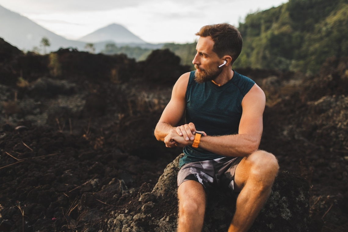 Man with wireless headphones looking at his fitness watch on a mountain