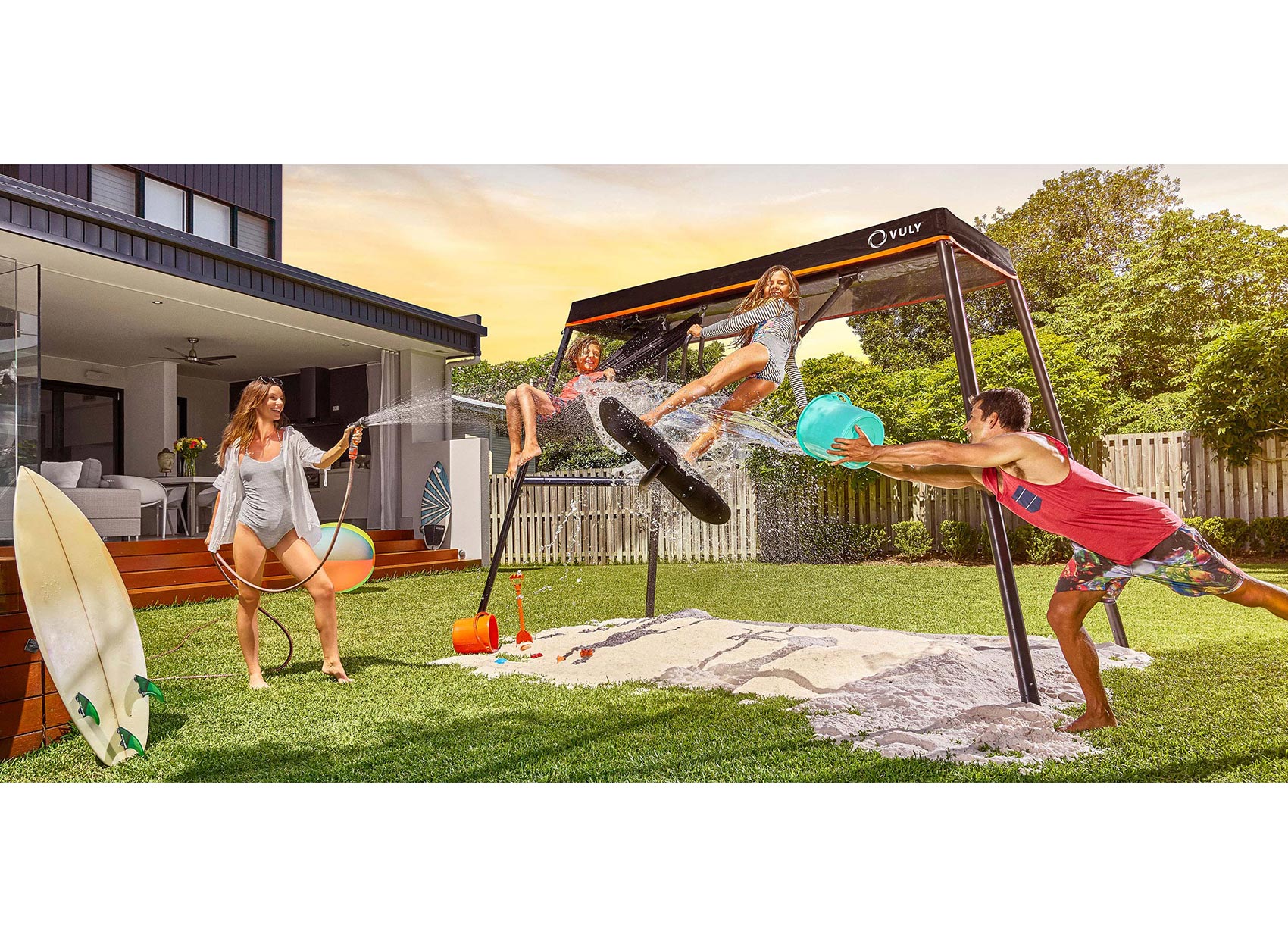 Children and parents playing and splashing water on their Vuly swing set in their backyard.